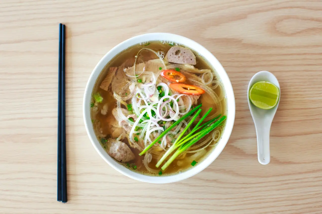 Bowl of pho soup with noodles, meat, herbs, and a side of lime and chopsticks Bowl of pho soup with noodles, meat, herbs, and a side of lime and chopsticks